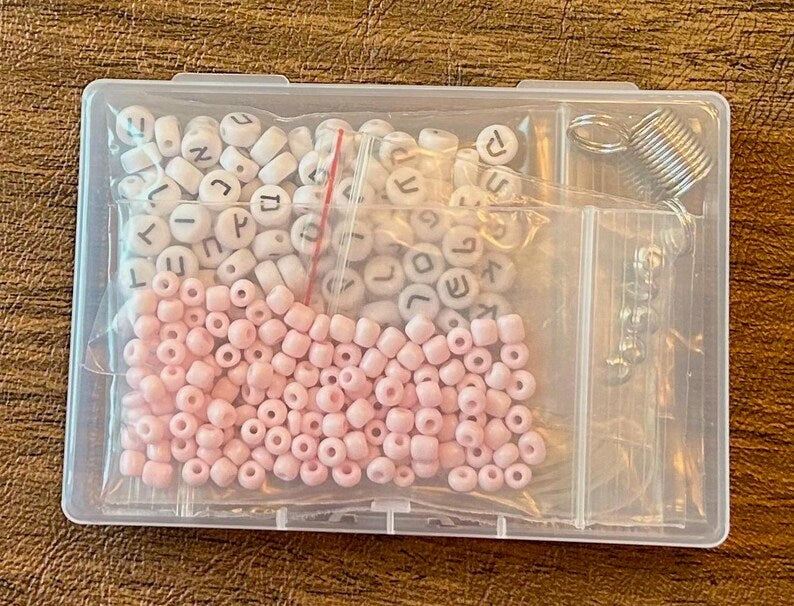 DIY Hebrew letter bracelet making kit by Pretty Beans featuring seed beads, silver charms, and tools for creating personalized jewelry.