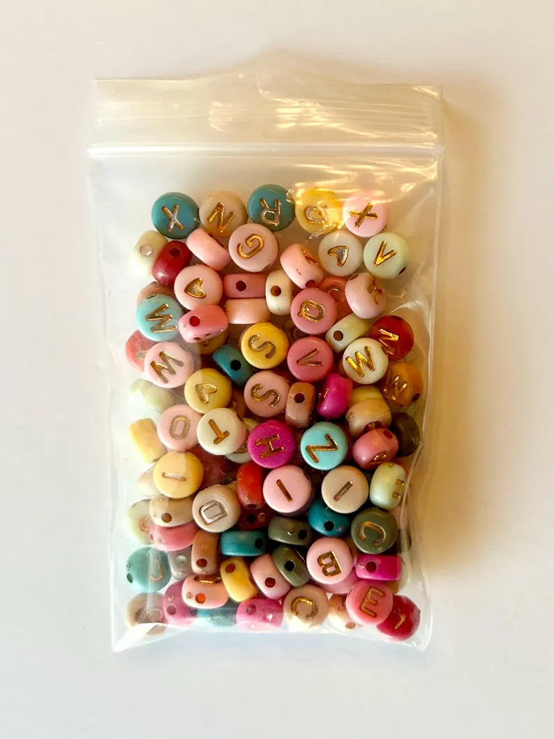 DIY jewelry kit by Pretty Beans featuring seed beads, letter charms, and silver charms for creating mini bracelets.