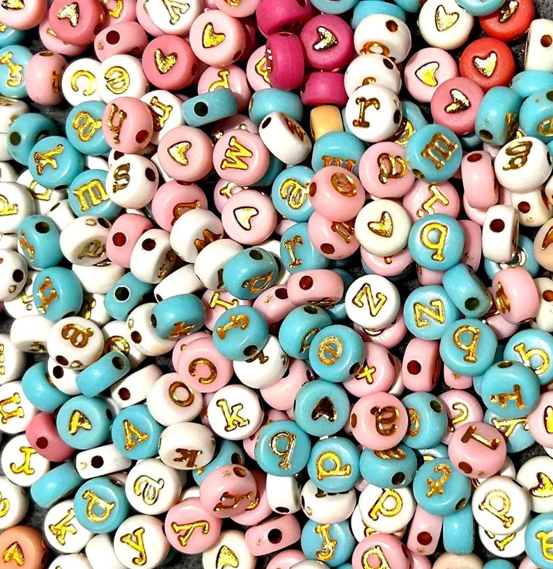 Lowercase gold alphabet beads with 7mm typewriter font for jewelry making, shown strung together in a close-up image.