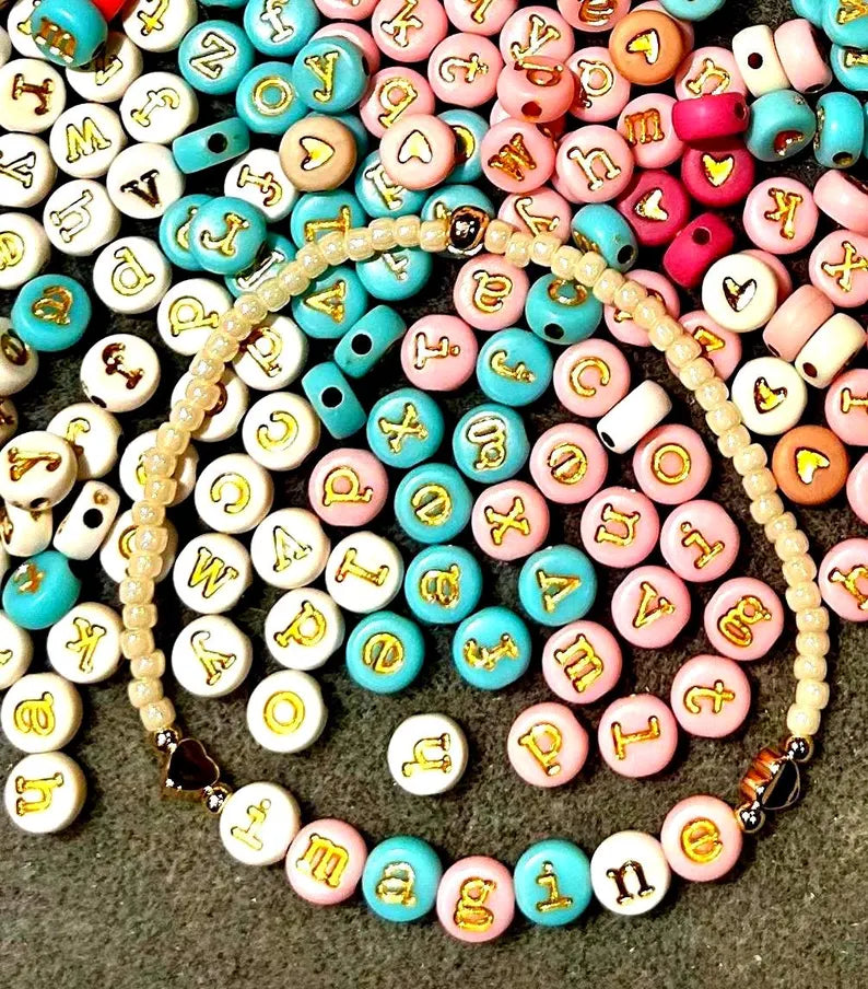 Gold lowercase alphabet beads featuring 7mm typewriter font for jewelry making, shown in a close-up image.