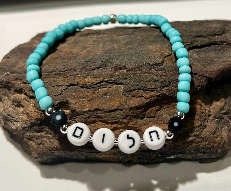 DIY Hebrew letter bracelet making kit with seed beads and silver charms by Pretty Beans, featuring colorful beads and jewelry supplies.