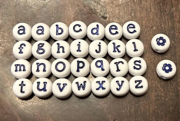 White lowercase alphabet beads with 7mm blue letter engravings, designed for jewelry making by Pretty Beans.