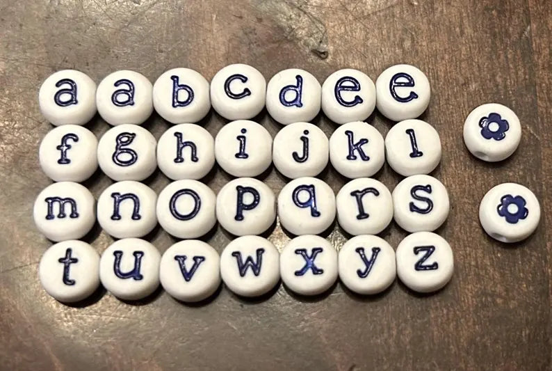 White lowercase alphabet beads with 7mm blue letter engravings, designed for jewelry making by Pretty Beans.