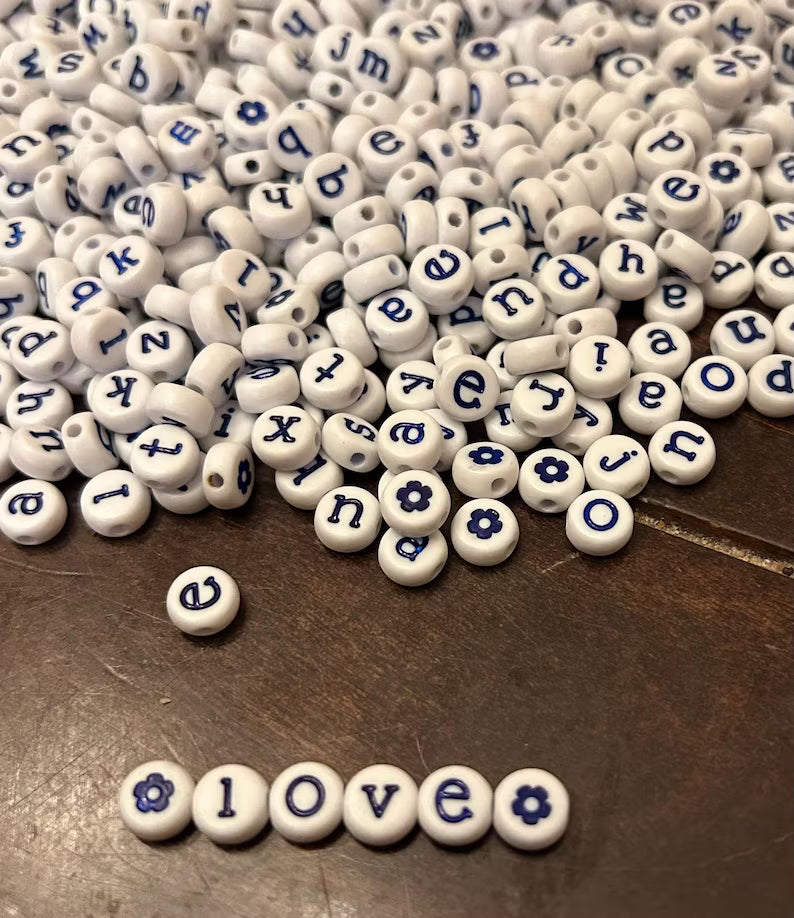 White lowercase alphabet beads with blue letters, 7mm size, from Pretty Beans, arranged in a cluster.