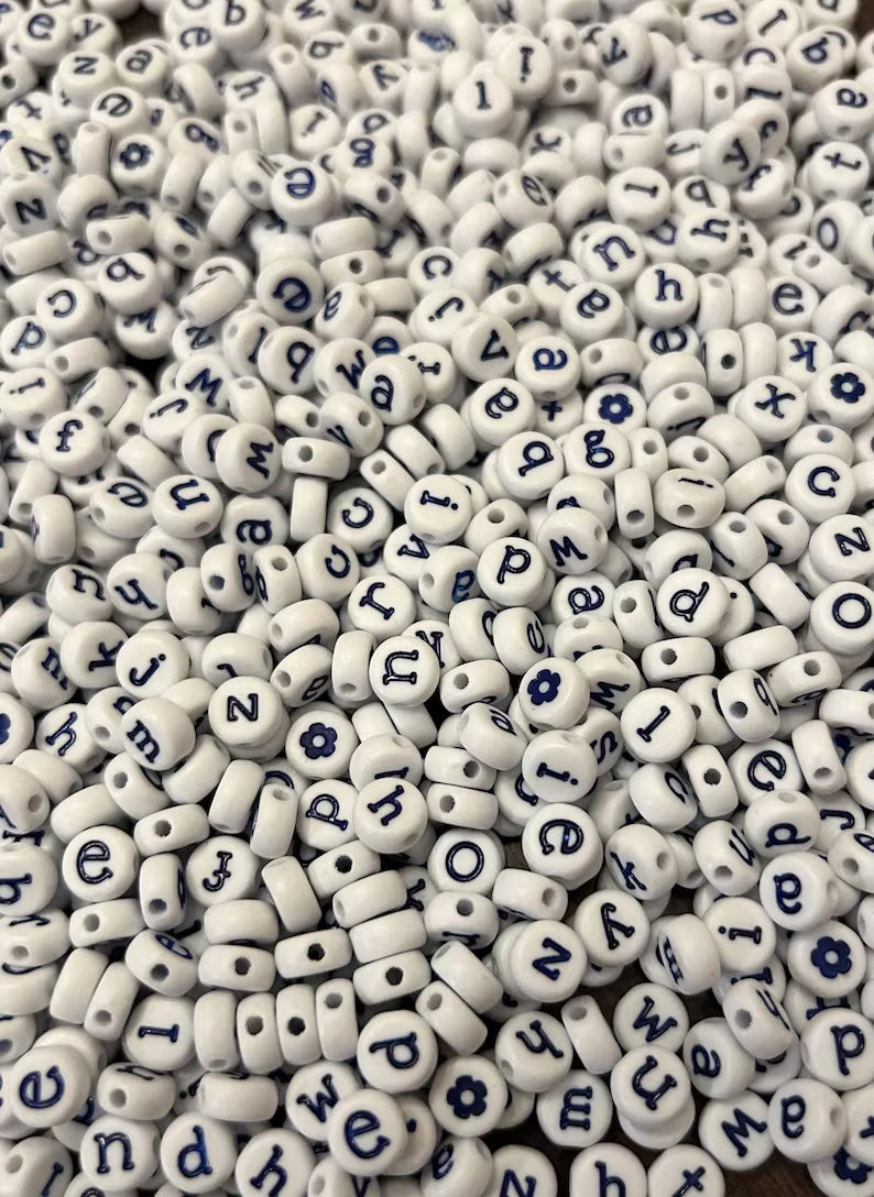 White lowercase alphabet beads with blue letters, 7mm size, from Pretty Beans, shown in a close-up image.