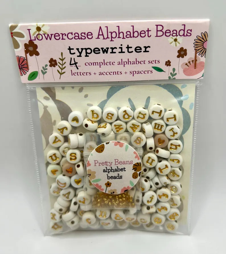 Lowercase gold alphabet beads with 7mm typewriter font for jewelry making, shown in a close-up image.
