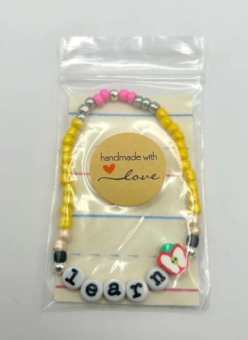 DIY teacher bracelet making kit by Pretty Beans with seed beads, letter beads, and apple charms on a white background.