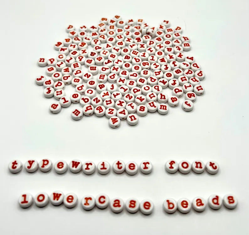 Lowercase orange typewriter font alphabet beads by Pretty Beans for jewelry making, shown in close-up detail.