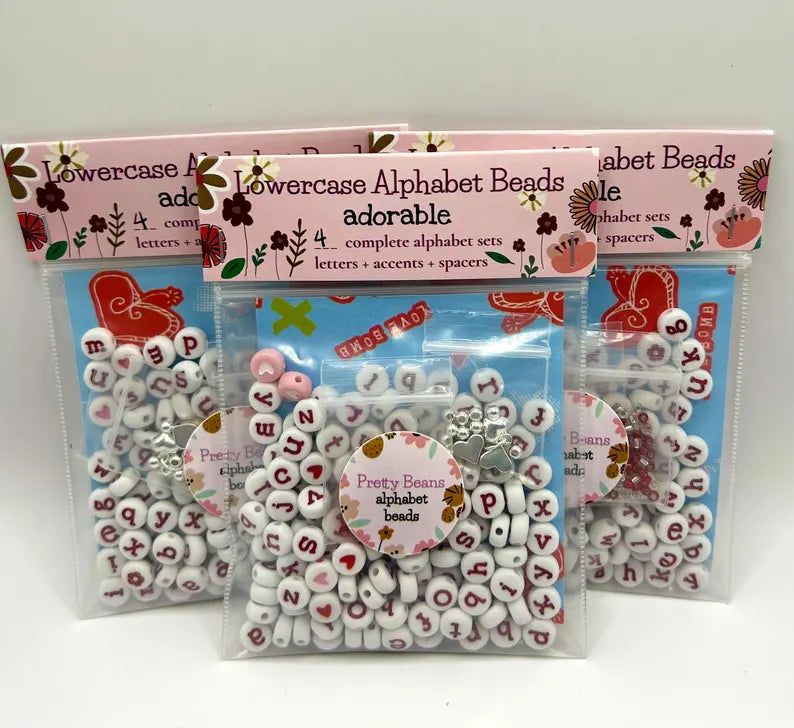 Red alphabet beads with silver accents for jewelry making, featuring letter shapes and vibrant color, by Pretty Beans.
