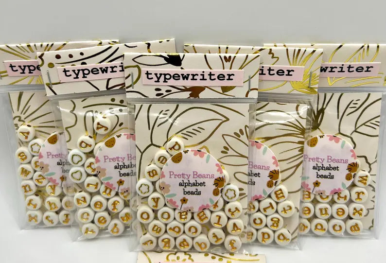 Lowercase gold alphabet beads with 7mm typewriter font for jewelry making, shown in a close-up image.