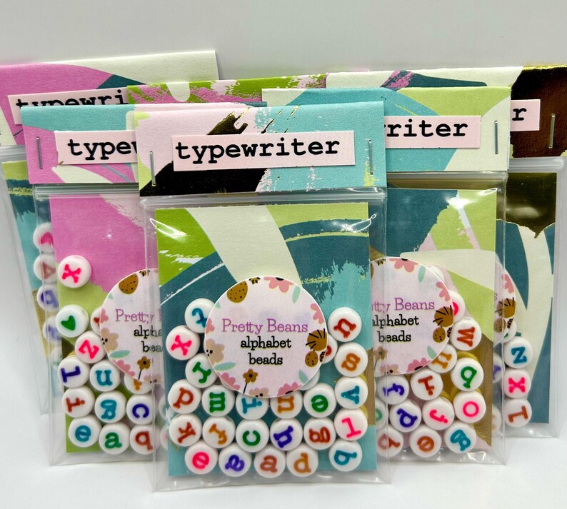 Colorful lowercase alphabet beads with typewriter font, 7mm size, arranged in a pile showcasing vibrant, multi-colored beads by Pretty Beans.